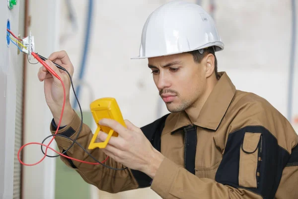 Eletricista verificando tensão de soquete usando multímetro em um dispositivo elétrico de parede — Fotografia de Stock