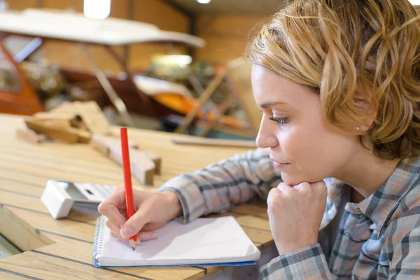 Schöne junge Tischlerin macht sich Notizen in ihrer Werkstatt — Stockfoto