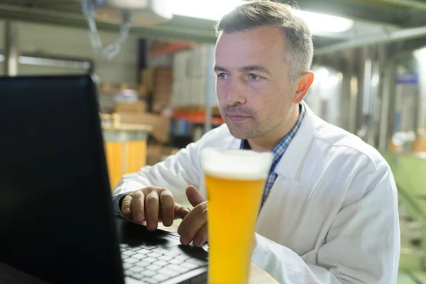 Пивовар, що працює з ноутбуком на виробництві — стокове фото