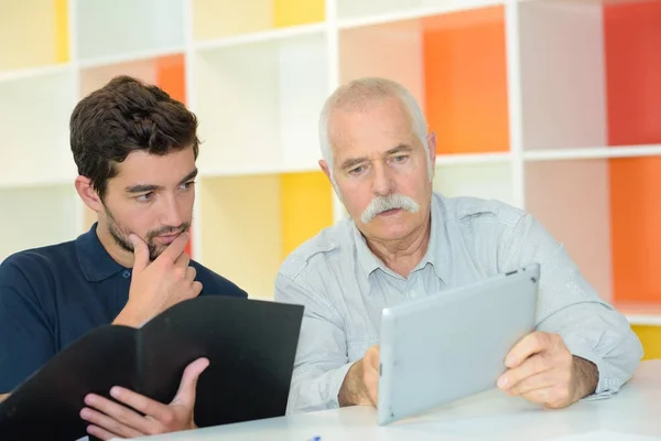 Zwei Männer in Besprechung halten Ordner in der Hand und schauen auf Tablet — Stockfoto