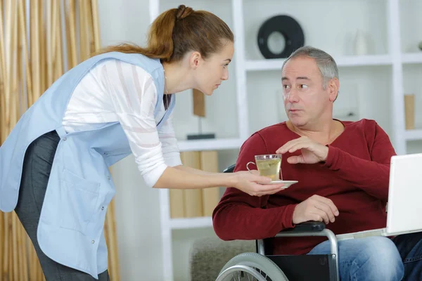 Cuidador sirviendo comida al hombre en silla de ruedas en casa —  Fotos de Stock