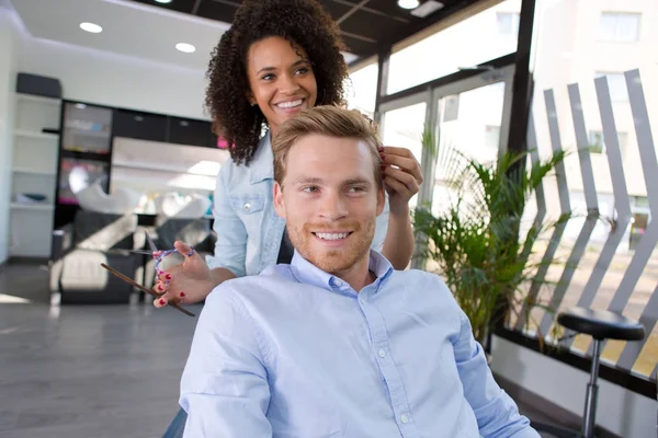 Female hairdresser is cutting hair of bearded man client — Stock Photo, Image