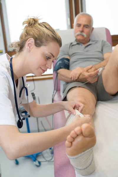 Bonito médico bandagem sênior mans ferido perna — Fotografia de Stock