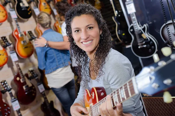 Volwassen vrouwelijke klant probeert af te spelen op nieuwe gitaar in winkel — Stockfoto