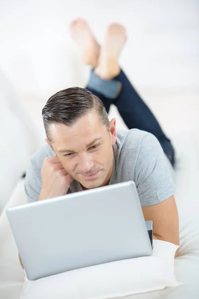 躺在沙发上使用笔记本电脑的成熟快乐的人 — 图库照片