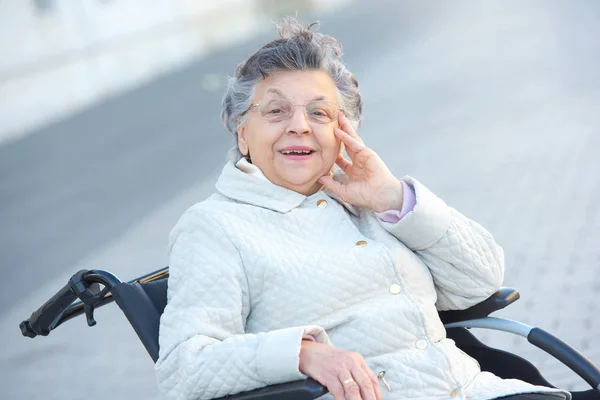 Mulher velha em cadeira de rodas ao ar livre sorrindo — Fotografia de Stock