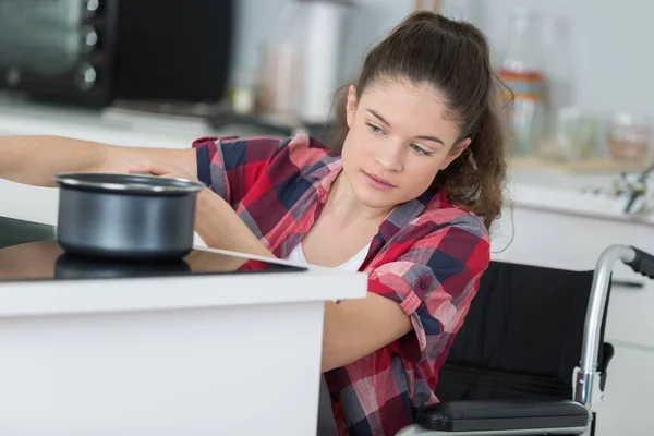 Mulher deficiente em cadeira de rodas preparando refeição na cozinha — Fotografia de Stock