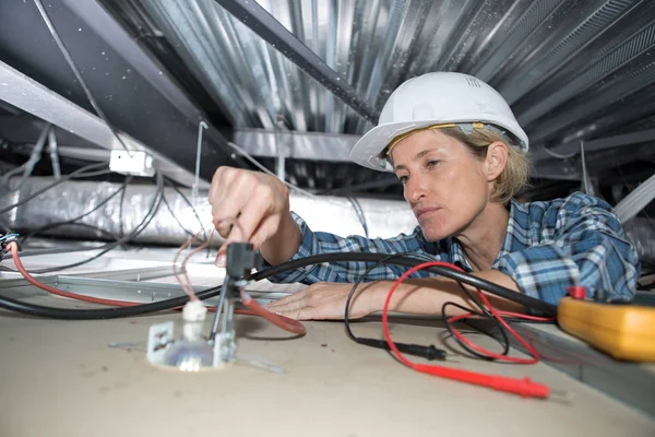 Vrouwelijke elektricien installeert elektrisch apparaat in plafond — Stockfoto