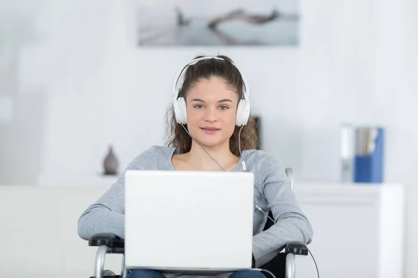 Χαρούμενα απενεργοποιημένη νεαρή γυναίκα που χρησιμοποιούν φορητό υπολογιστή στο αναπηρικό αμαξίδιο στο σπίτι — Φωτογραφία Αρχείου