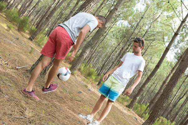Två män som spelar fotboll i tallskogen — Stockfoto