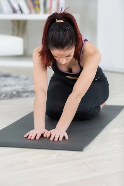 Женщина растягивает тело на коврике для йоги дома — стоковое фото