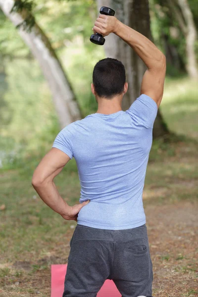 Hombre con los brazos levantados haciendo ejercicios de elevación con pesas — Foto de Stock