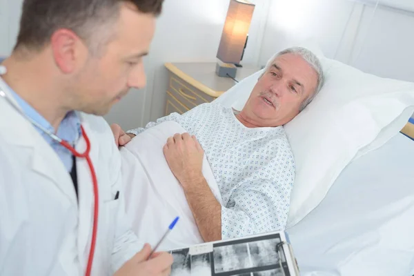 Männlicher Arzt, der neben dem Patienten steht und Ergebnisse hält — Stockfoto