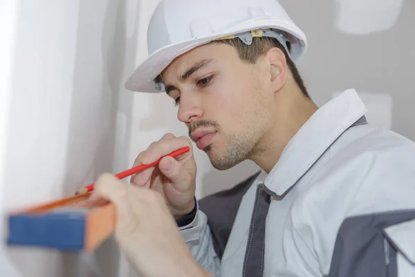 Male construction worker marking on wooden plank at home — Stock Photo, Image