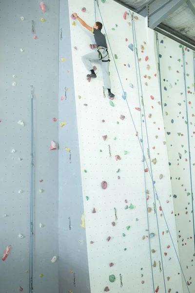 Ampla vista da escalada masculina em uma parede de escalada interior — Fotografia de Stock