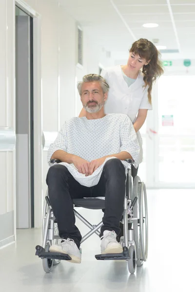 Hombre discapacitado en silla de ruedas mientras una enfermera lo empuja —  Fotos de Stock