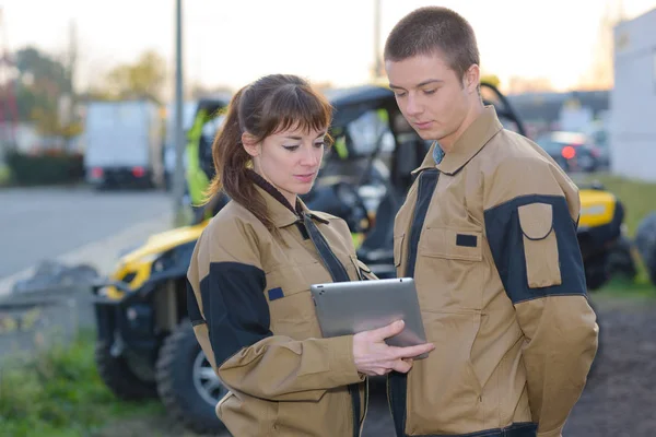 Mechanics looking at computer tablet in front of parked quads — стоковое фото