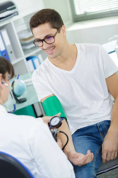 Jovem paciente bonito recebendo sua pressão arterial verificada — Fotografia de Stock