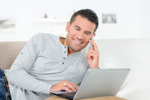 Χαμογελαστός άνθρωπος χρησιμοποιώντας φορητό υπολογιστή και κινητό τηλέφωνο — Φωτογραφία Αρχείου