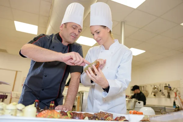 Vezető séf figyeli a segédje, egy tál díszítéshez — Stock Fotó