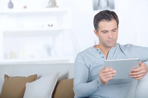 Schöner Mann surft auf dem Tablet auf der Couch — Stockfoto