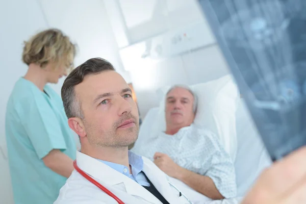 Врач смотрит на рентген, пациент на заднем плане — стоковое фото