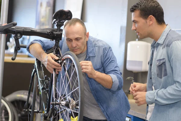 Vendedor hablando con el cliente mientras fija la rueda de bicicleta —  Fotos de Stock