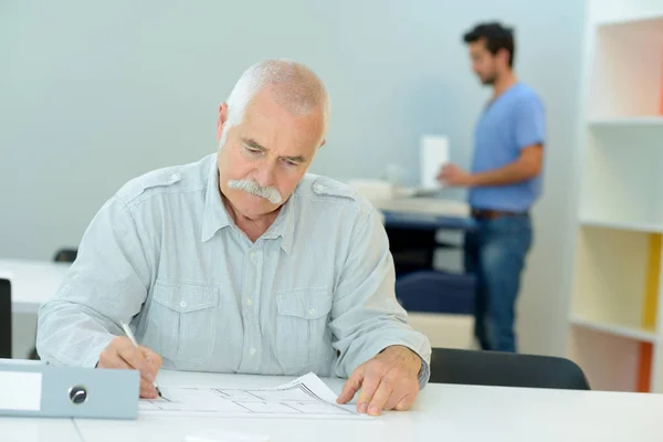 Hombre mayor sentado en el escritorio llenando el papeleo —  Fotos de Stock