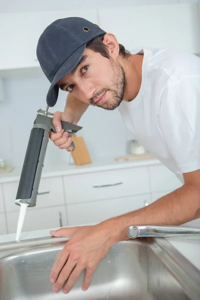 Uomo che applica silicone intorno lavello della cucina — Foto Stock