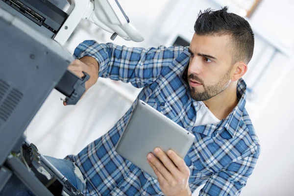 Technician using a tablet to fix a printer — Stock Photo, Image