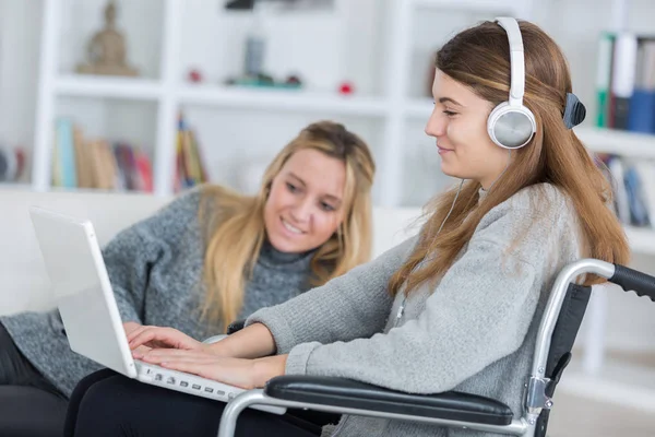 Invalid girl on the wheelchair with laptop with a friend — Stock Photo, Image