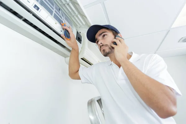 Young handyman repairing air conditioning system calling for help — Stock Photo, Image