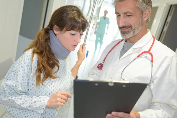 Lächelnder Arzt zeigt Röntgenbild einer Patientin mit Halskrause — Stockfoto