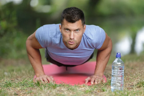 Man doing push ups on grass in summer park — Stock Photo, Image