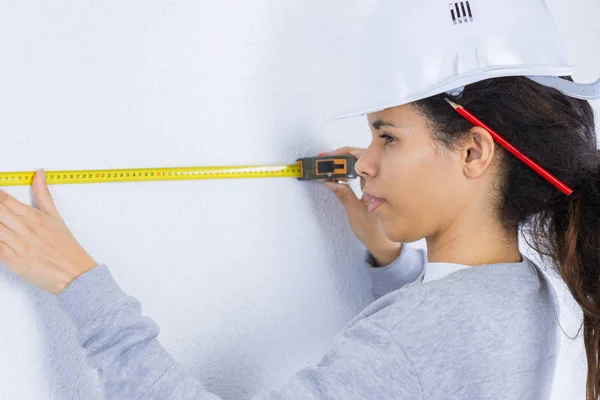 Jovem mulher medindo uma parede com fita métrica — Fotografia de Stock