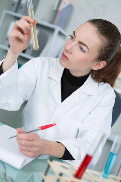 Científica femenina inspeccionando el tubo tst y tomando notas — Foto de Stock