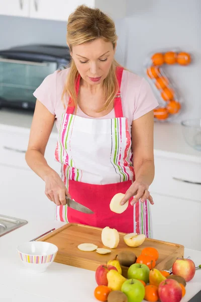 Femme plus âgée épluchant des pommes dans sa cuisine — Photo