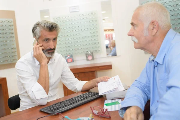 Opticien aidant le patient masculin âgé avec de nouvelles lunettes — Photo