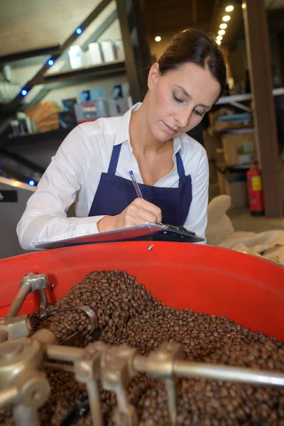 コーヒー ロースト マシンの横にメモをとる女性 — ストック写真