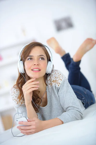 Молода жінка лежить на ліжку і слухає музику — стокове фото