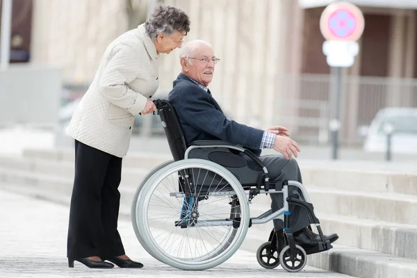 Senior homme en fauteuil roulant être poussé par femme — Photo