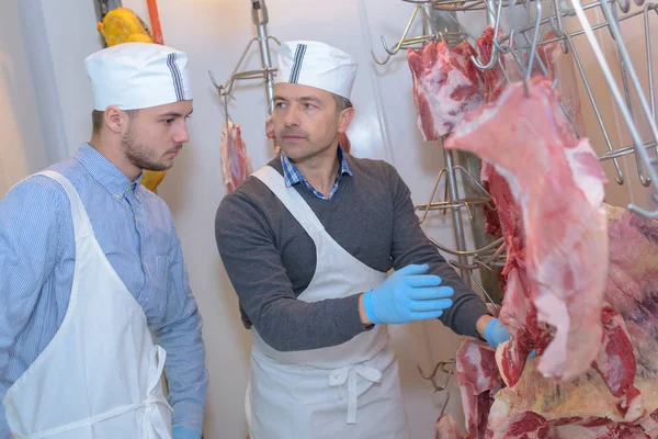 Carniceiro sênior mostrando carcaças de animais para carniceiro júnior — Fotografia de Stock