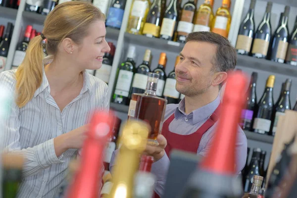 Venditore dando bottiglia di liquore al cliente femminile — Foto Stock