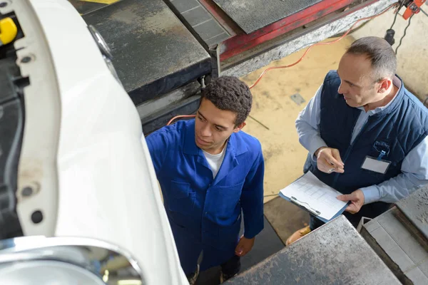 Mécanicien qualifié en salopette travaillant sous une voiture relevée — Photo