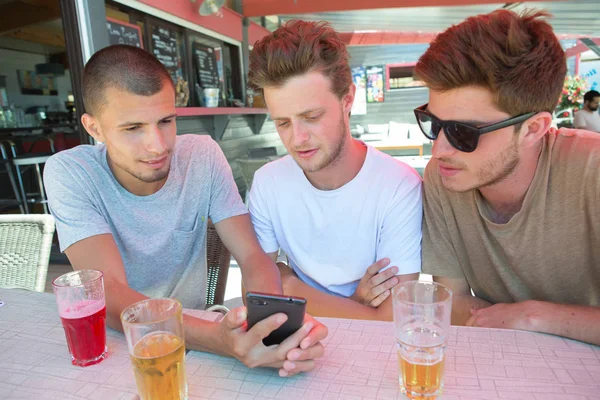 Трое друзей-мужчин расслабляются и пьют пиво на террасе ресторана — стоковое фото