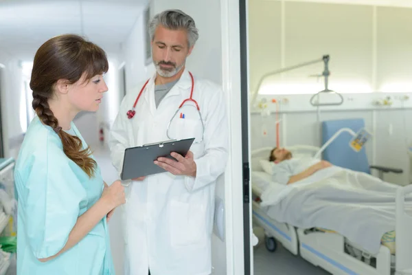 Trabajadores médicos mirando el portapapeles fuera de la habitación del paciente —  Fotos de Stock