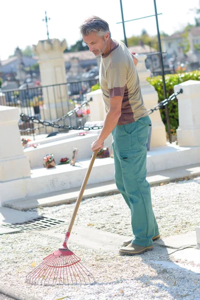 Zelador raking no cemitério — Fotografia de Stock