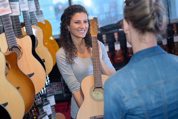 Frau präsentiert Akustikgitarre im Geschäft — Stockfoto