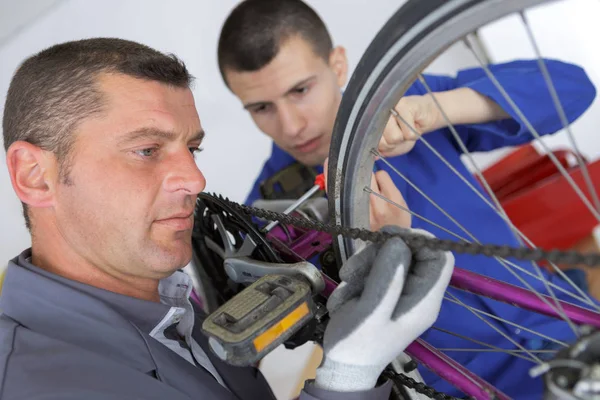 Mecânico de bicicletas e aprendiz reparar uma bicicleta na oficina — Fotografia de Stock