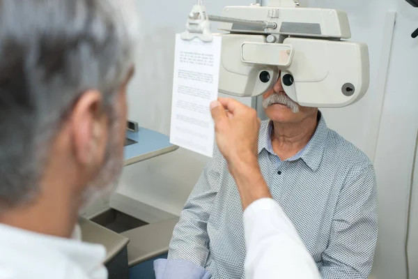 Beállító phoropter, vezető beosztású férfi beteg optometrista — Stock Fotó
